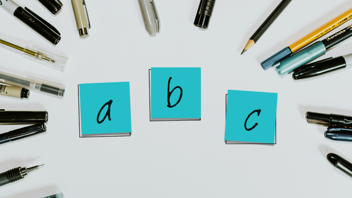 Three sticky notes, a b c, surrounded by writing instruments.