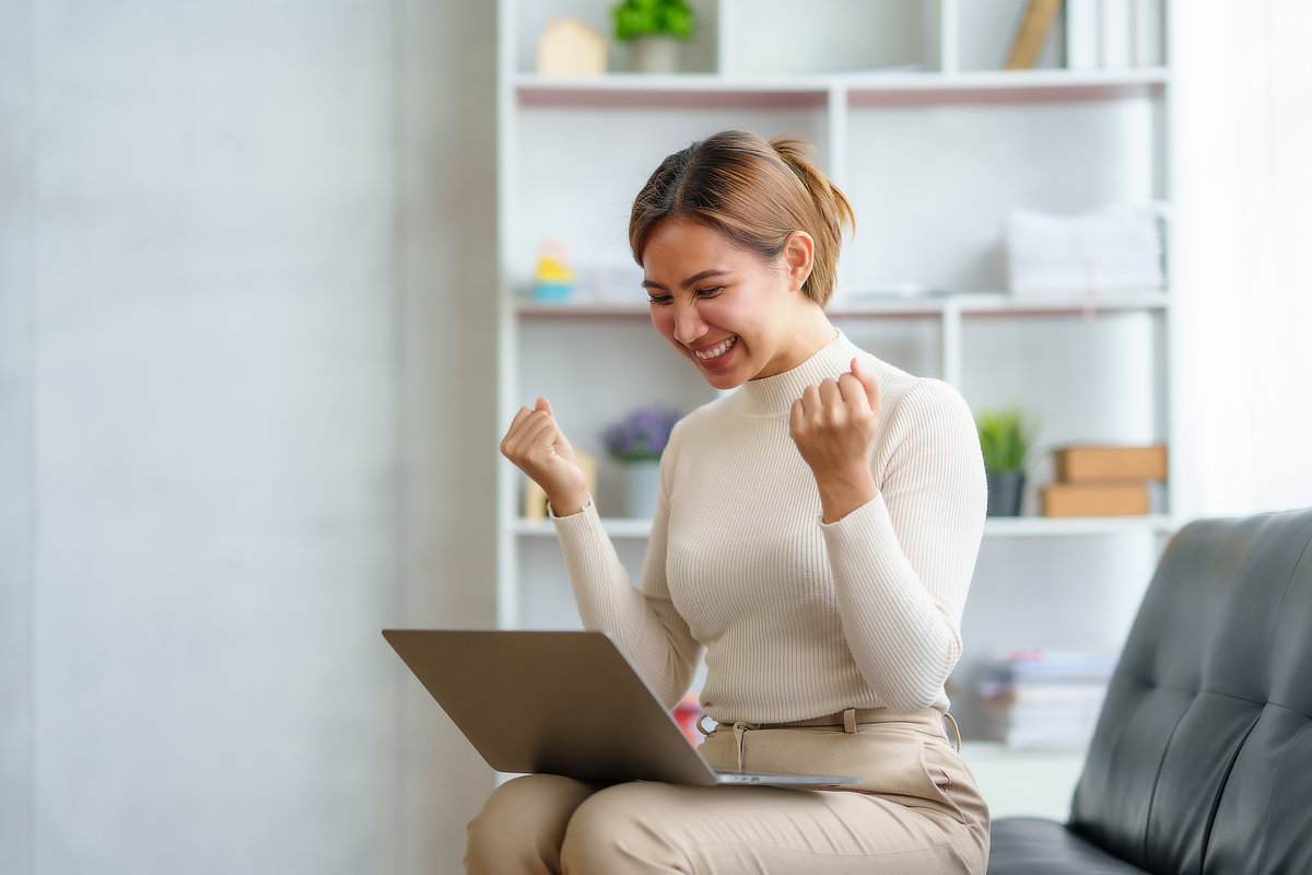 Woman with hands raised in celebration in front of laptop